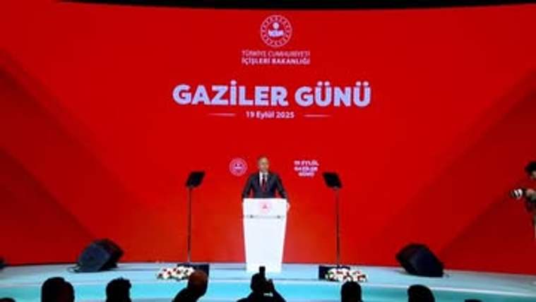 Kırmızı sahnede “Gaziler Günü” yazılı fonda, kürsüde konuşan bir kişi ve önünde izleyiciler görülüyor.