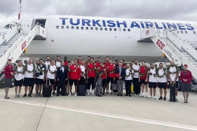 Türk Hava Yolları uçağının önünde, madalyalı sporcular ve görevliler birlikte poz veriyor.