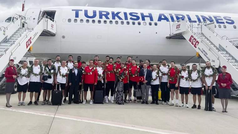 Türk Hava Yolları uçağının önünde, madalyalı sporcular ve görevliler birlikte poz veriyor.