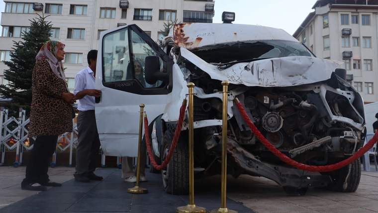 Ön kısmı hasar görmüş beyaz bir minibüs, etrafında kırmızı halı ve zincirle çevrilmiş.