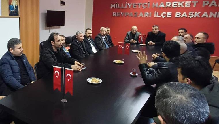 Toplantı masasında oturan bir grup insan, Türk bayrakları ve duvarda parti yazısıyla görülüyor.