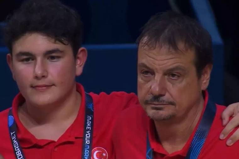 Kırmızı spor formaları giyen iki kişi yan yana duruyor; sağdaki kişinin gözleri dolu görünüyor.