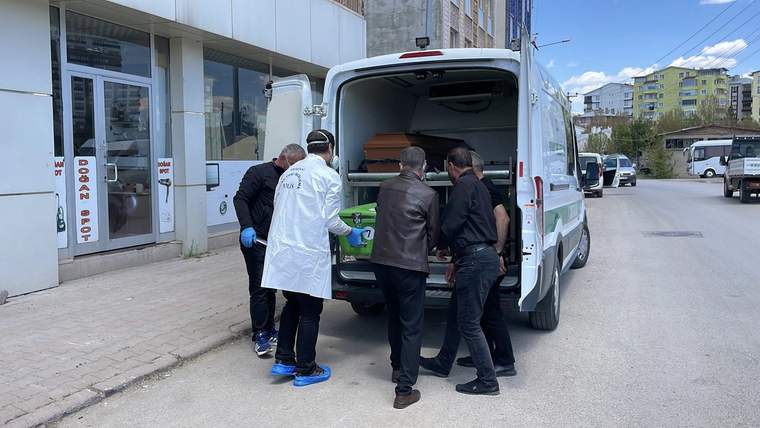 Beyaz önlüklü görevliler ve üç kişi, sokakta park halindeki ambulansın açık arka kapısında duruyor.