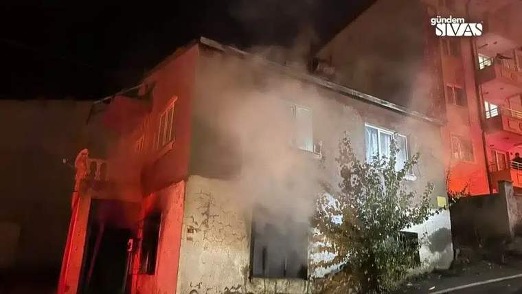 Bir binanın penceresinden duman çıkıyor, çevresinde ağaçlar var.