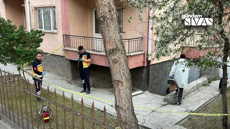 Apartman girişinin önünde üç kişi, sarı şeritler ve bir yangın tüpü görülüyor.