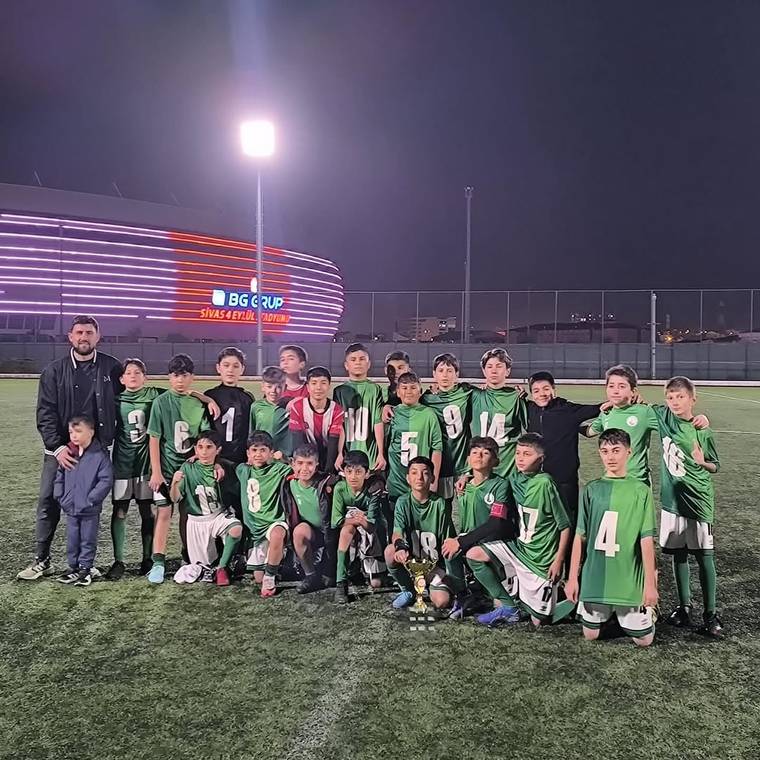 Gece aydınlatılan futbol sahasında yeşil formalı çocuklardan oluşan takım, toplu halde poz veriyor.