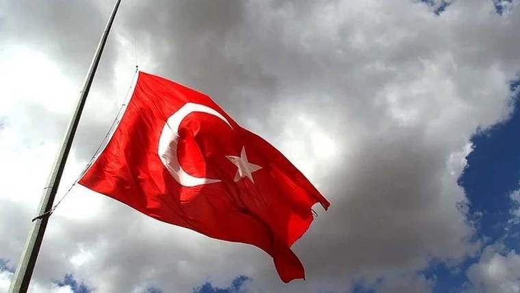 Yarısı yarıya çekilmiş Türk bayrağı, arka planda bulutlu bir gökyüzü ile görünmekte.