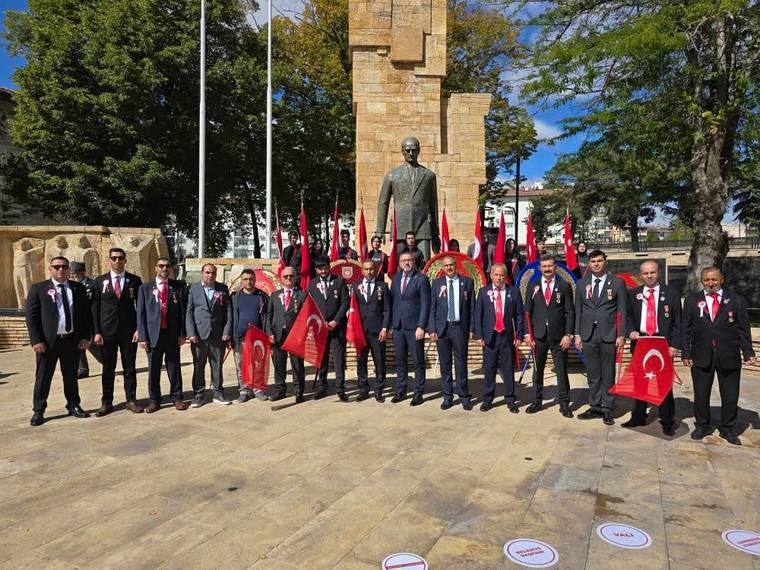 Taş kaide üzerindeki heykelin önünde takım elbiseli kişiler, Türk bayrakları ve flamalarla duruyor.