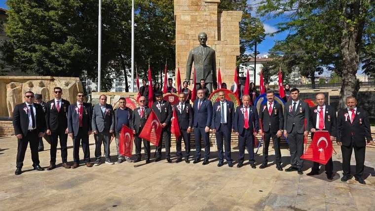 Taş kaide üzerindeki heykelin önünde takım elbiseli kişiler, Türk bayrakları ve flamalarla duruyor.