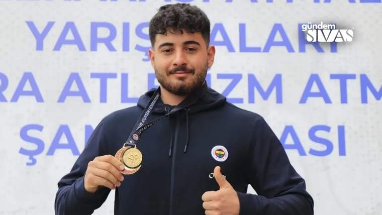 Altın madalya tutan bir genç sporcu, gülümseyerek parmağını yukarı kaldırıyor.