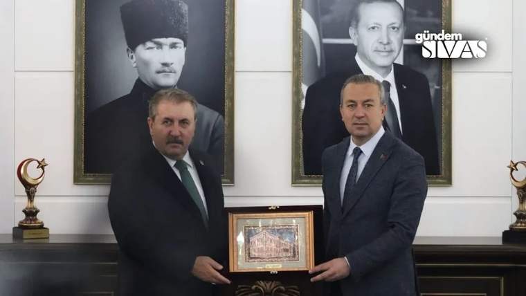 İki kişi, bir çerçeve içinde resim tutarak poz veriyor; arka planda üç portre var.