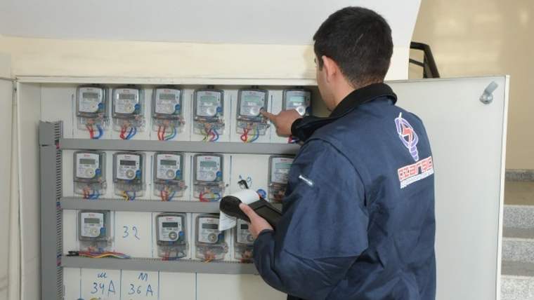 Bir teknisyen, duvara monteli elektrik sayaçlarından birinin okumasını yapıyor.