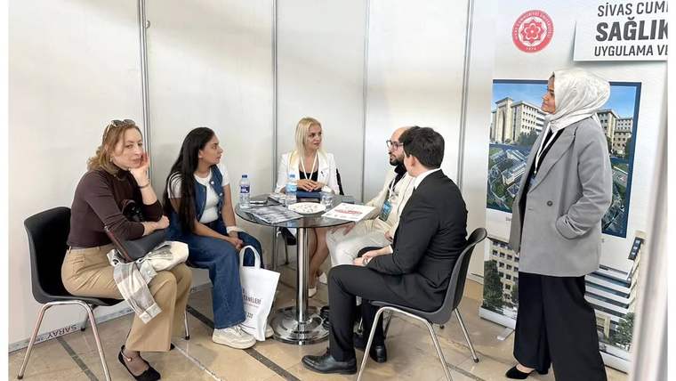 Bir stantta oturan beş kişi, sağlık turizmi hakkında sohbet ediyor. Arka planda Sivas Cumhuriyet Üniversitesi'nin logosu görünmekte.