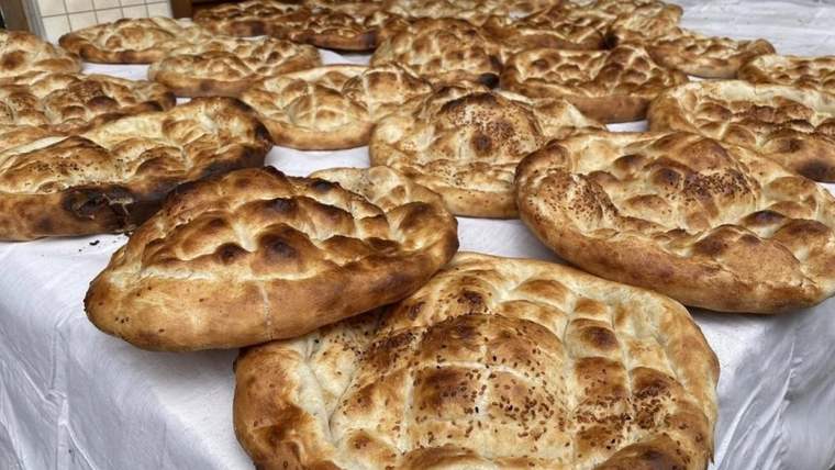 Beyaz örtü üzerinde susamlı ve kızarmış çok sayıda Ramazan pidesi üst üste duruyor.