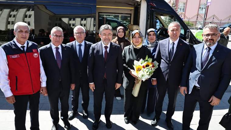 Bir grup insan, bir minibüsün önünde duruyor; bazıları çiçek tutuyor.