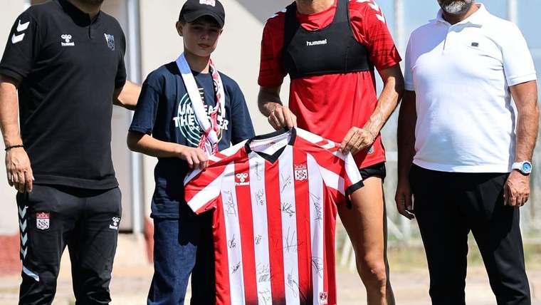 Üç yetişkin ve bir çocuğun önünde, kırmızı-beyaz çizgili futbol formasını tutan iki kişi görülüyor.
