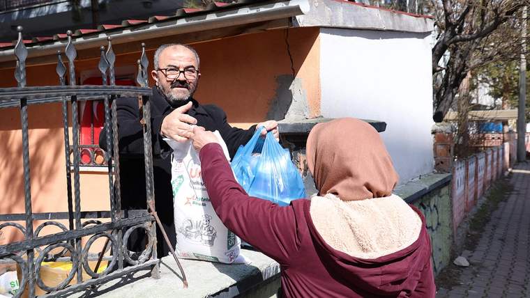 Bir kişi, kapıdan bir kadına poşetler uzatıyor; kadın poşetleri alıyor.