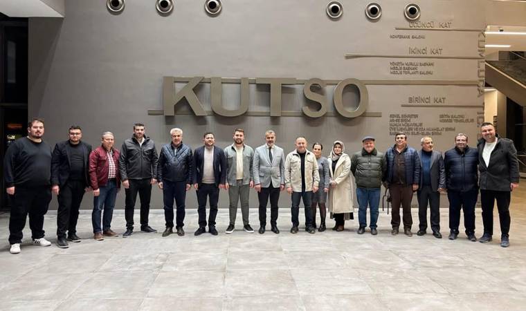 KUTSO yazısının önünde, iç mekânda yan yana duran bir grup kişi kameraya bakarak poz veriyor.