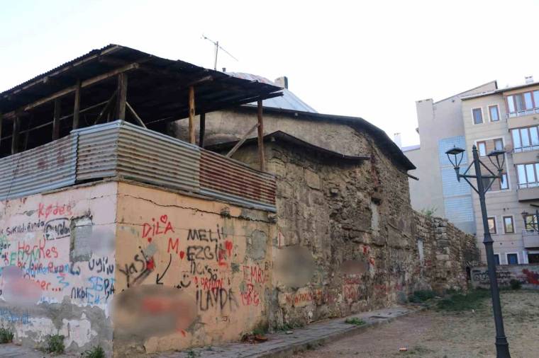 Grafitilerle kaplı, çatısı kısmen çökmüş eski yapı; yanında apartmanlar ve bir sokak lambası görülüyor.