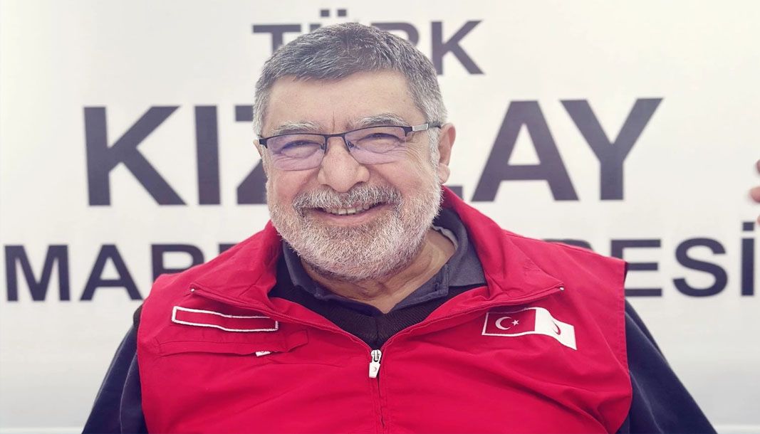 Kırmızı Kızılay montu giymiş, gülümseyen bir adam, arka planda Kızılay yazısı var.