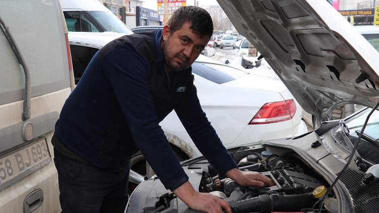 Bir adam, açık motor kaputunun önünde aracı tamir etmeye çalışıyor.