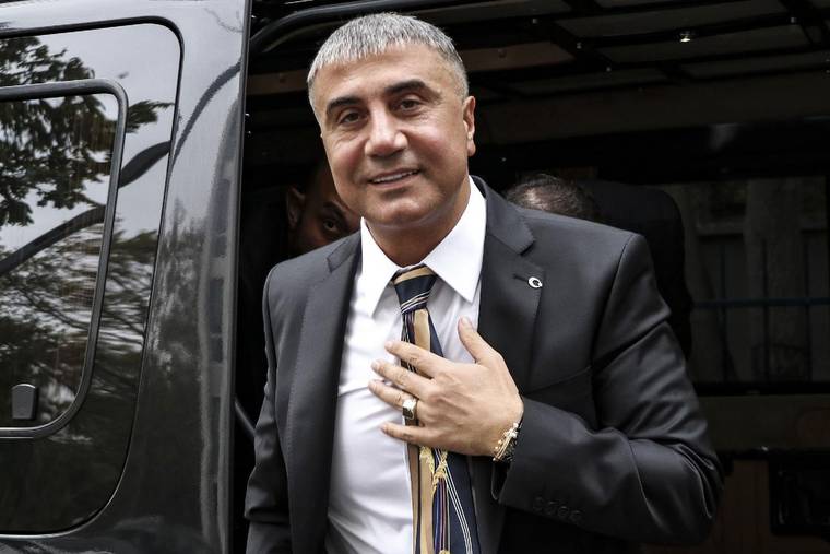 Takım elbiseli, gri saçlı bir kişi siyah bir aracın kapısından çıkarken elini göğsüne koyuyor.