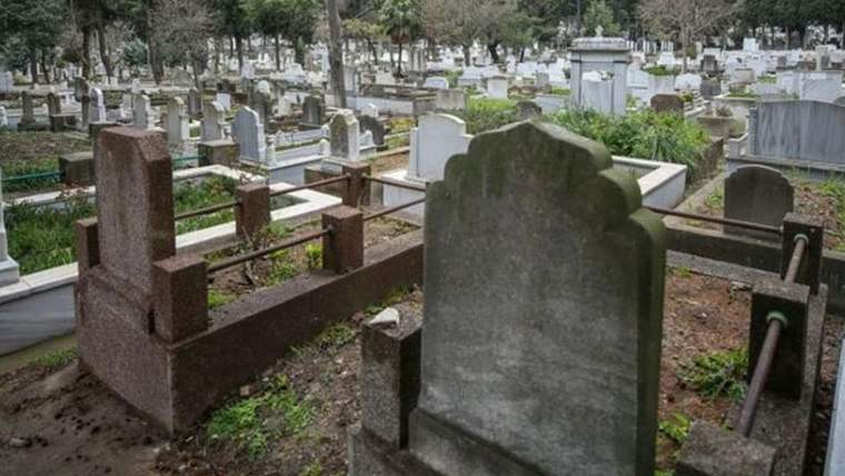 Mezarlıkta farklı biçimlerde mermer mezar taşları ve çevrelerini saran metal korkuluklar görülüyor.