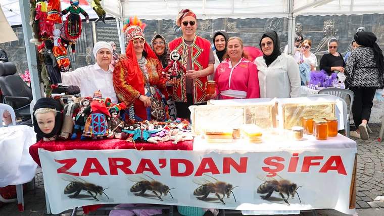Çadırdaki stantta yöresel kıyafetli kişiler, el işi ürünler ve kavanozlar sergileniyor; masada “Zara’dan Şifa” yazıyor.