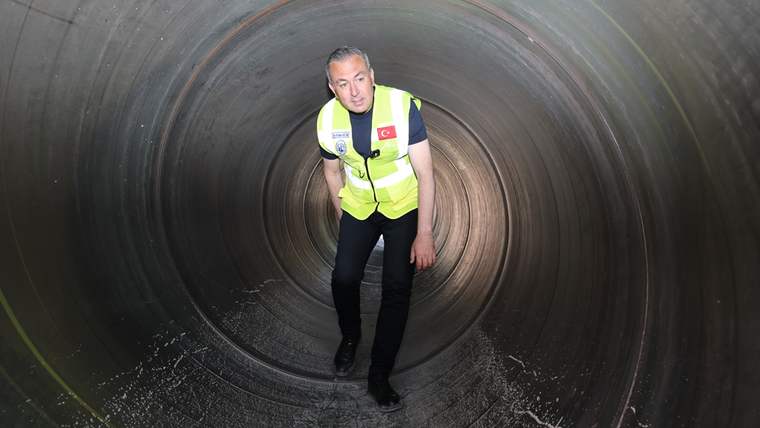 Reflektörlü yelek giyen bir kişi, geniş çaplı beton bir borunun içinde ayakta duruyor.