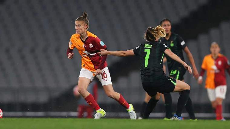 Turuncu-kırmızı formalı futbolcu top sürerken, siyah formalı rakibi savunma hamlesi yapıyor.