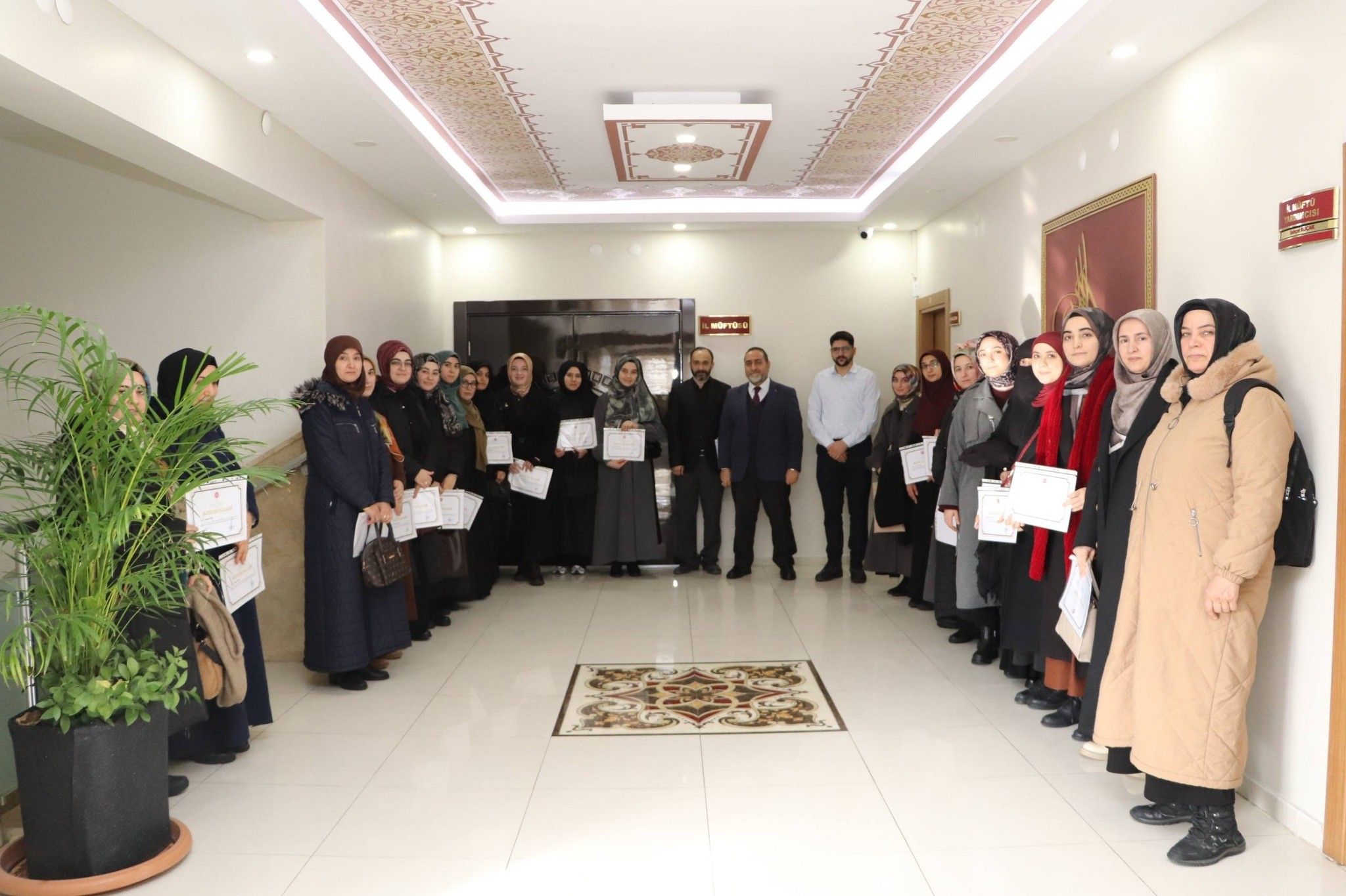 Koridorda bir araya gelen kadın ve erkeklerden oluşan grup, ellerinde belgelerle birlikte duruyor.
