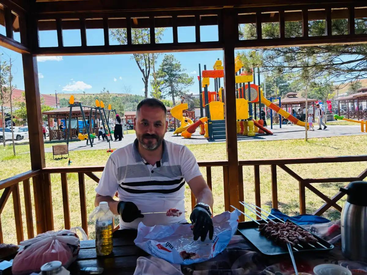 Ahşap kamelyada oturan bir kişi, önündeki masada şiş kebap, içecek ve piknik malzemeleriyle görülüyor.