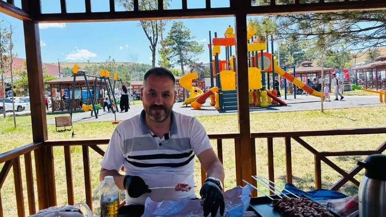 Ahşap kamelyada oturan bir kişi, önündeki masada şiş kebap, içecek ve piknik malzemeleriyle görülüyor.