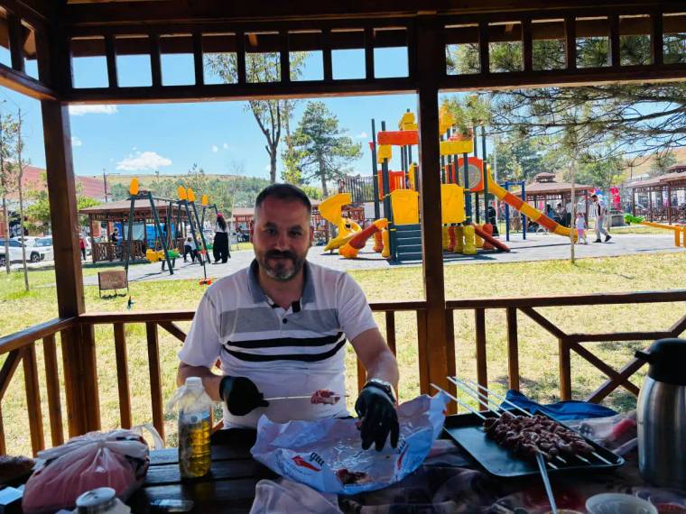 Ahşap kamelyada oturan bir kişi, önündeki masada şiş kebap, içecek ve piknik malzemeleriyle görülüyor.