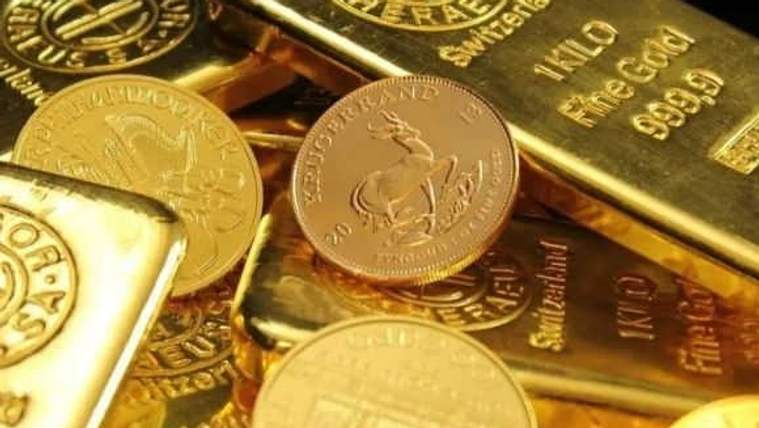 Üst üste duran altın külçeleri ve madeni paralar; külçelerin üzerinde “999.9 FINE GOLD” yazıyor.