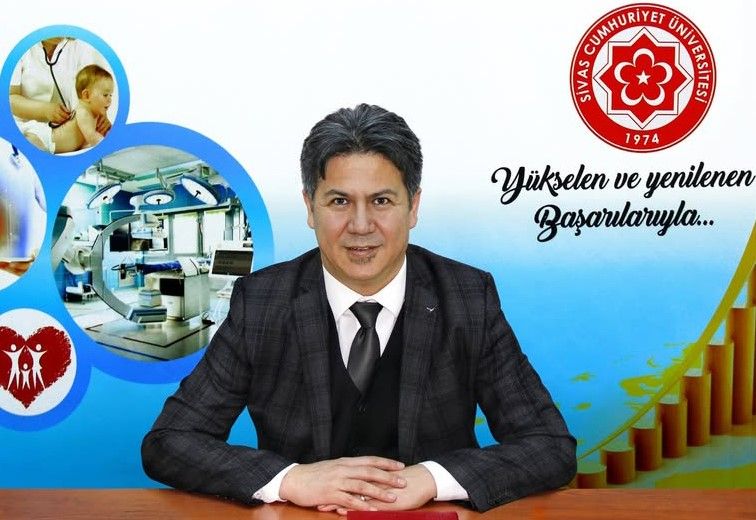 Sivas Cumhuriyet Üniversitesi logosunun bulunduğu arka planda, masada oturan bir kişi gülümsüyor.