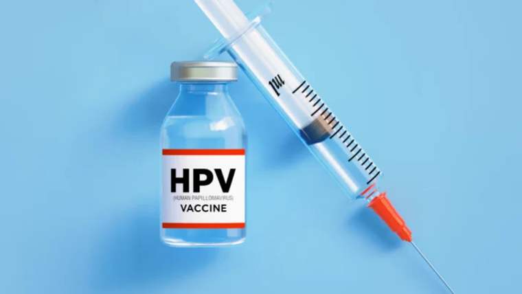 Mavi zeminde, üzerinde HPV Vaccine yazan aşı şişesi ve yanında duran enjektör görülüyor.