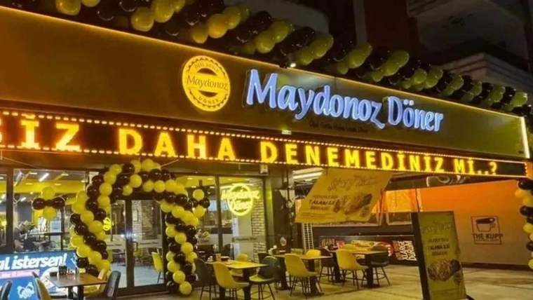Maydonoz Döner tabelalı restoranın girişinde sarı ve siyah balon süslemeleri, dışarıda masa ve sandalyeler görülüyor.