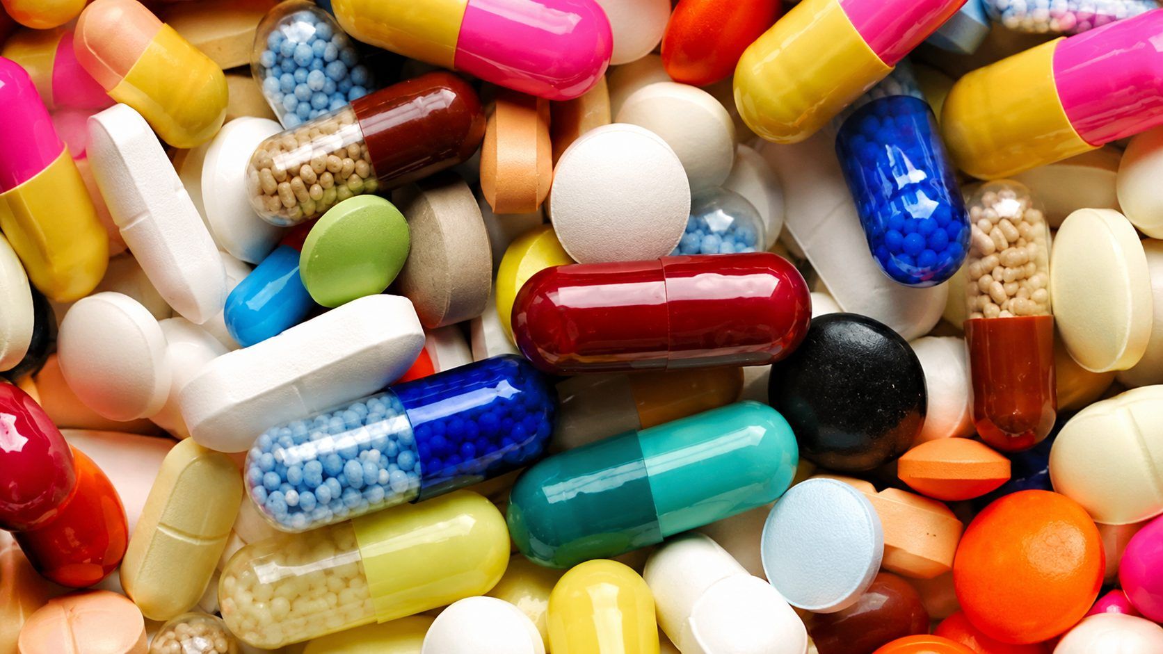 Çeşitli renk ve biçimlerde kapsül, tablet ve drajelerin birbirinin üzerine dizildiği yakın plan görünüm.