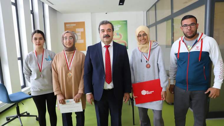 Dört kişi, bir adamın etrafında duruyor; hepsi gülümseyerek poz veriyor.