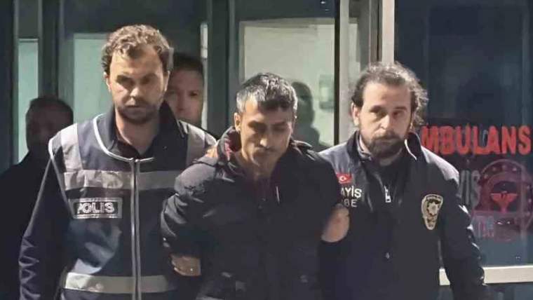 İki polis memuru, bir kişiyi kelepçeli olarak hastane çıkışında götürüyor.