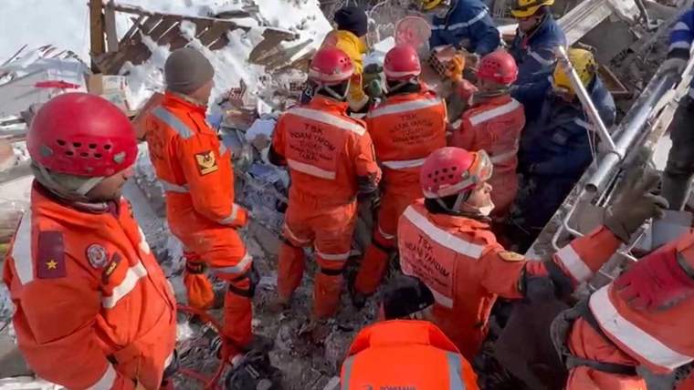 Kırmızı kask takan ve turuncu kıyafet giyen arama kurtarma ekipleri, enkaza müdahale ediyor.