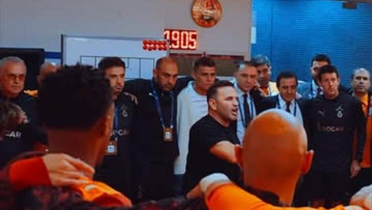 Galatasaray logosunun bulunduğu salonda, turuncu formalı kişilerin çevrelediği bir grup görülüyor.