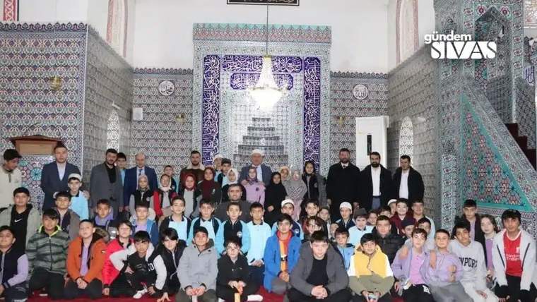 Çini kaplı bir ibadet mekânında, çocuklar ve yetişkinlerden oluşan kalabalık toplu halde duruyor.
