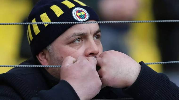 Fenerbahçe forması giymiş bir taraftar, üzgün bir şekilde ellerini ağzına kapamış.