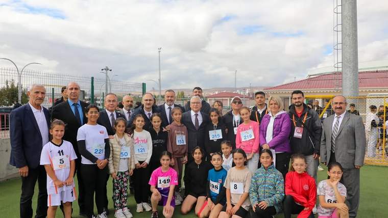 Açık hava spor alanında, numaralı formalar giyen çocuklar ve yetişkinler toplu halde poz veriyor.