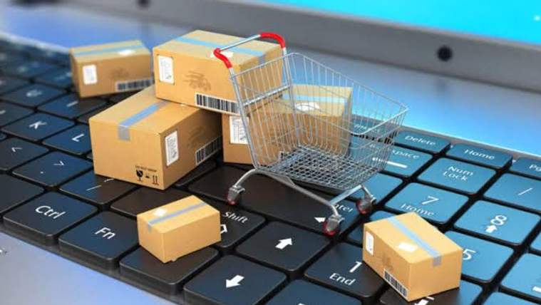 Bir bilgisayar klavyesinin üzerinde, içinde kutular bulunan bir alışveriş sepeti ve paketler yer alıyor.