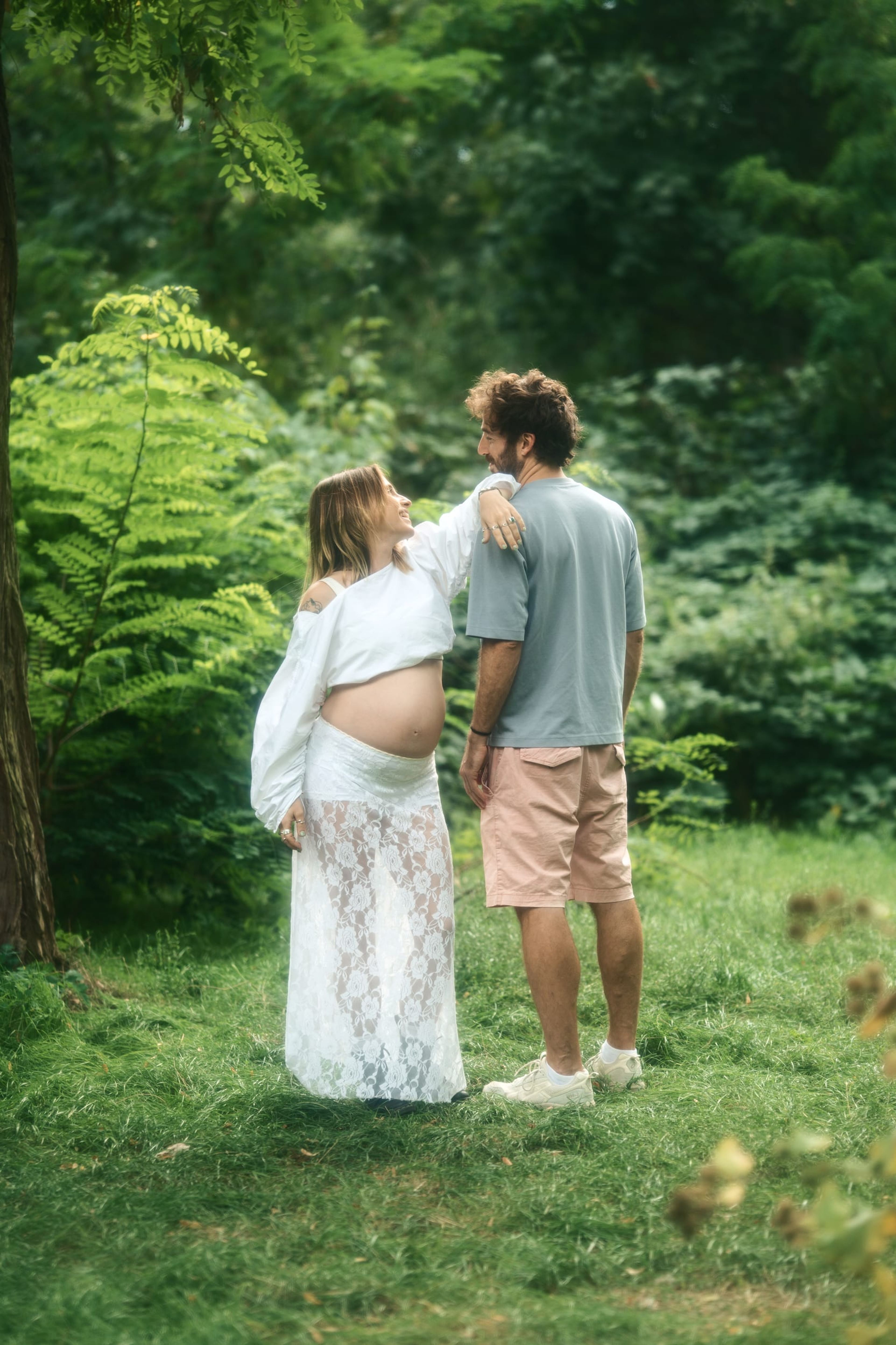 Expectant couple standing together in the park, her arm around his shoulder
