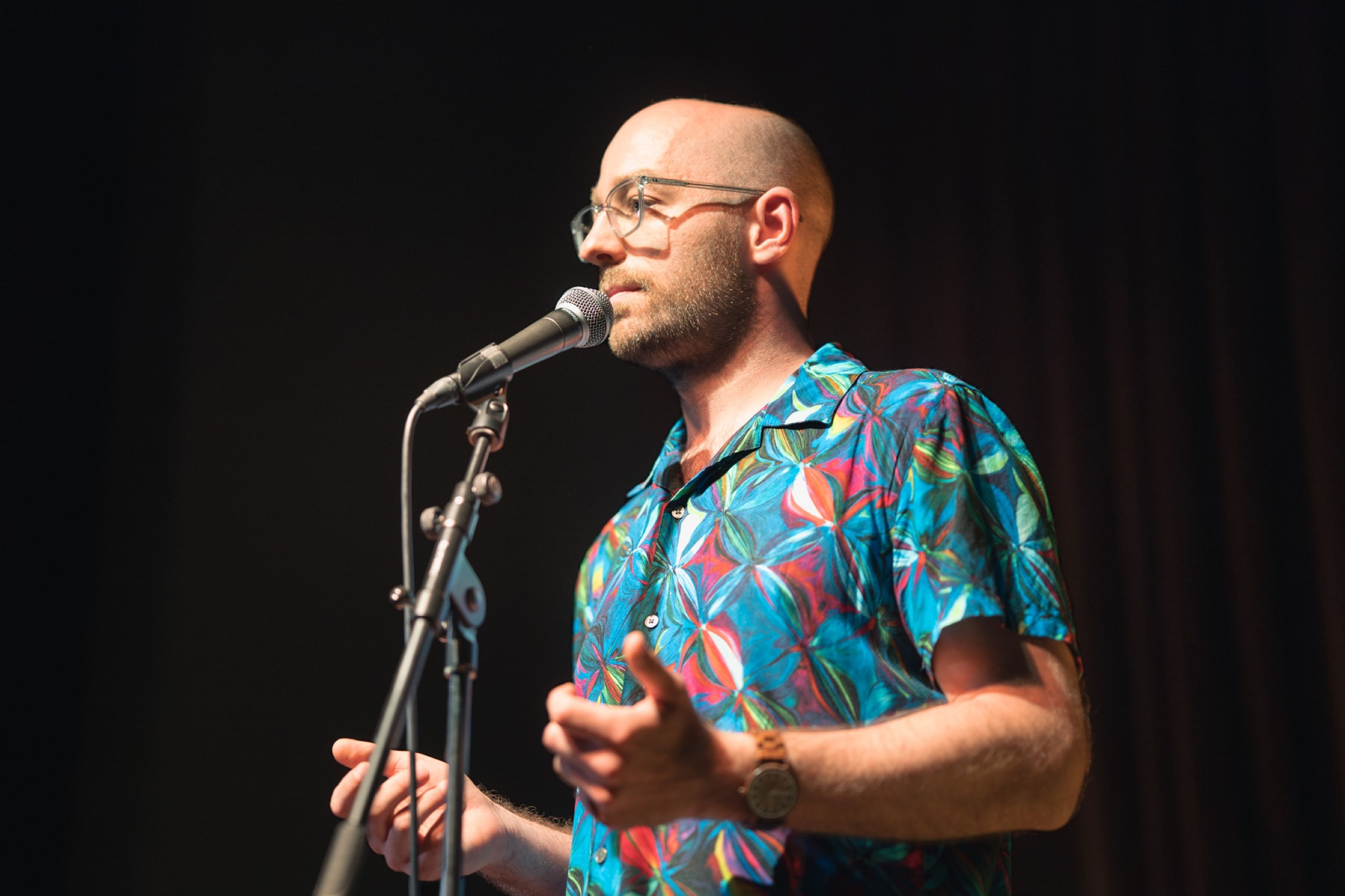 Storyteller in a bright floral shirt speaking into the microphone