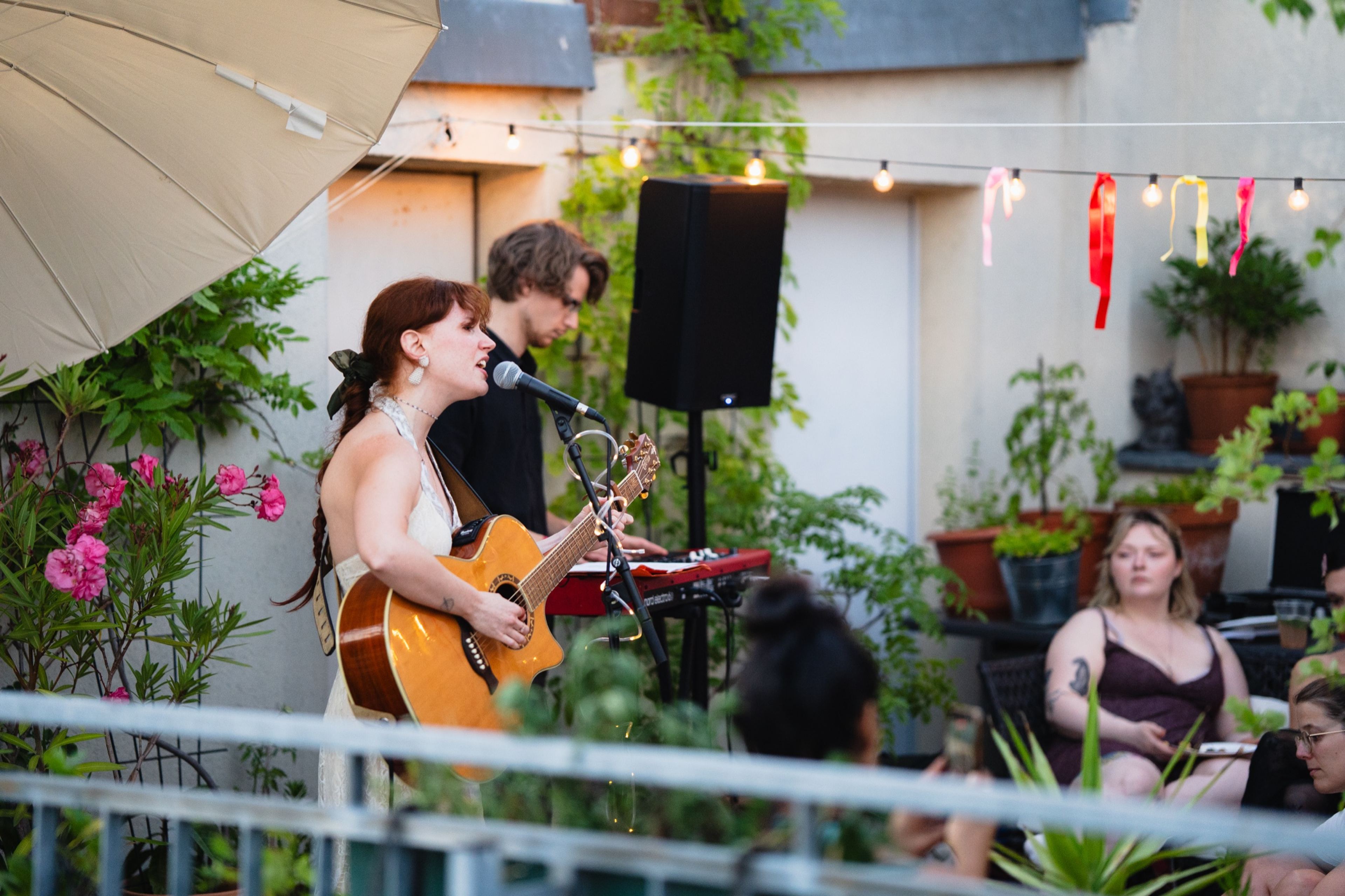 Rooftop stage with singer, guitarist and keyboardist under festoon lights at a Her Sound concert in Berlin